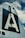 The image features the vertical stabilizer of an aircraft, prominently displaying a large letter 'A' against a dark background. The structure appears metallic with visible rivets, set against a partly cloudy sky.