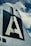 The image features the vertical stabilizer of an aircraft, prominently displaying a large letter 'A' against a dark background. The structure appears metallic with visible rivets, set against a partly cloudy sky.