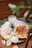 Heart-shaped waffles with berry syrup are placed on a white plate surrounded by pale pink and white roses. A decorative glass, containing a clear liquid and a slice of lemon, sits nearby. The wooden surface adds a rustic charm.