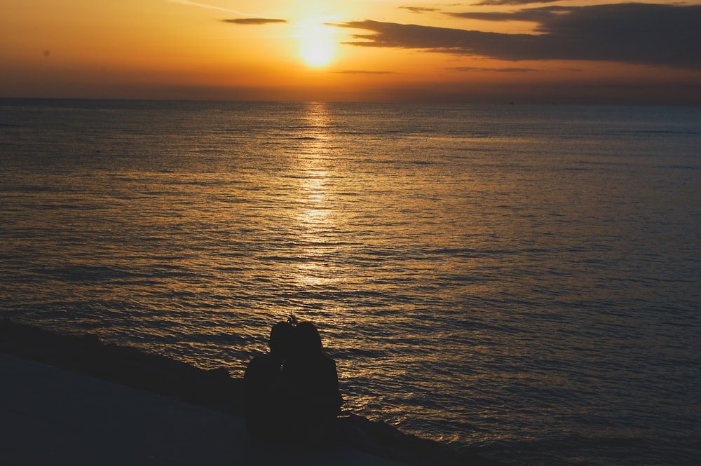 silhouette of man and woman sitting on rock during sunset