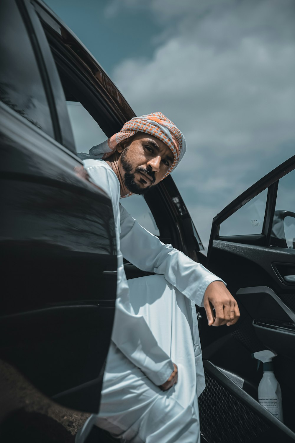 man in white thobe standing beside black car during daytime