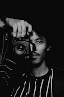 man in black and white crew neck shirt holding black nikon dslr camera