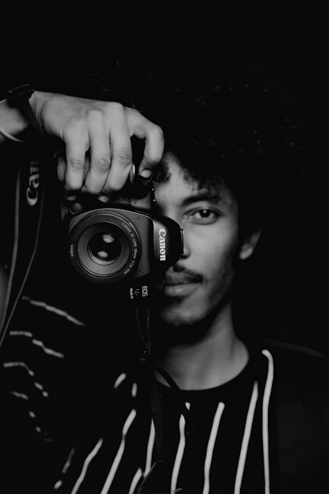 man in black and white crew neck shirt holding black nikon dslr camera