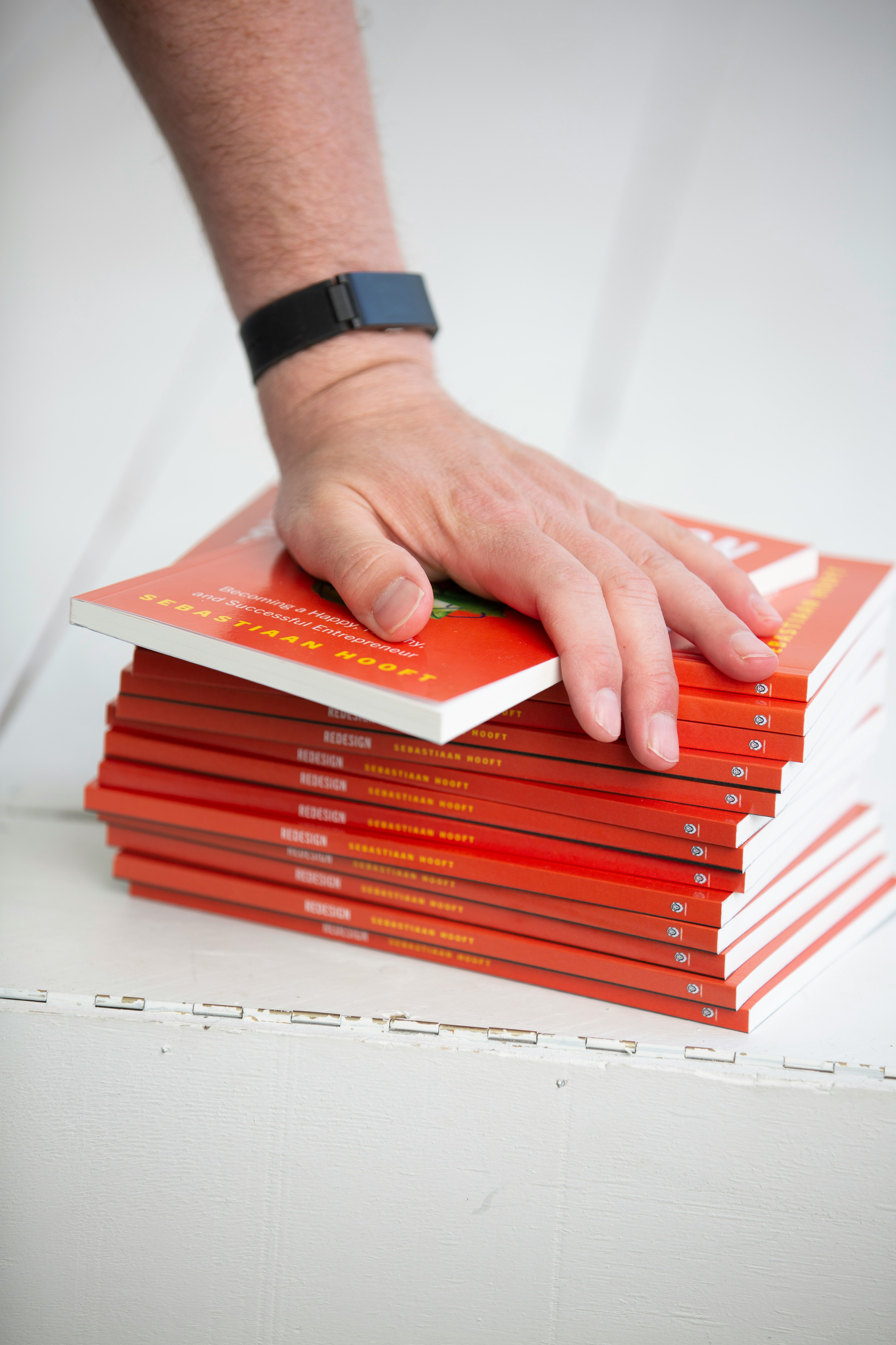 Author Sebastiaan Hooft has his hand on a pile of Redesign books, wearing Withings fitness tracker.