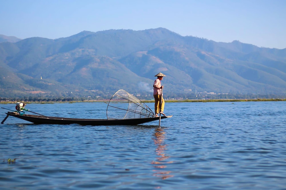Femme en chemise blanche et chapeau brun debout sur un bateau sur un plan d’eau pendant la journée