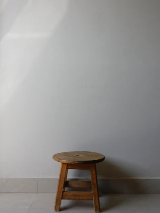 A rustic wooden bench stool placed against a white brick wall with soft natural light