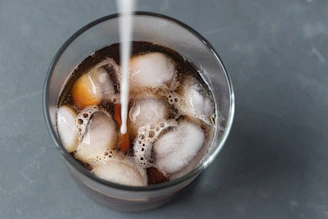 clear drinking glass with iced coffee being sweetened with cream