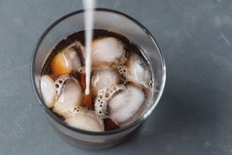 clear drinking glass with iced coffee being sweetened with cream