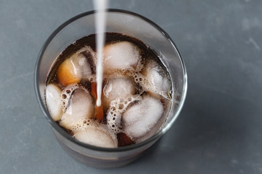 clear drinking glass with iced coffee being sweetened with cream