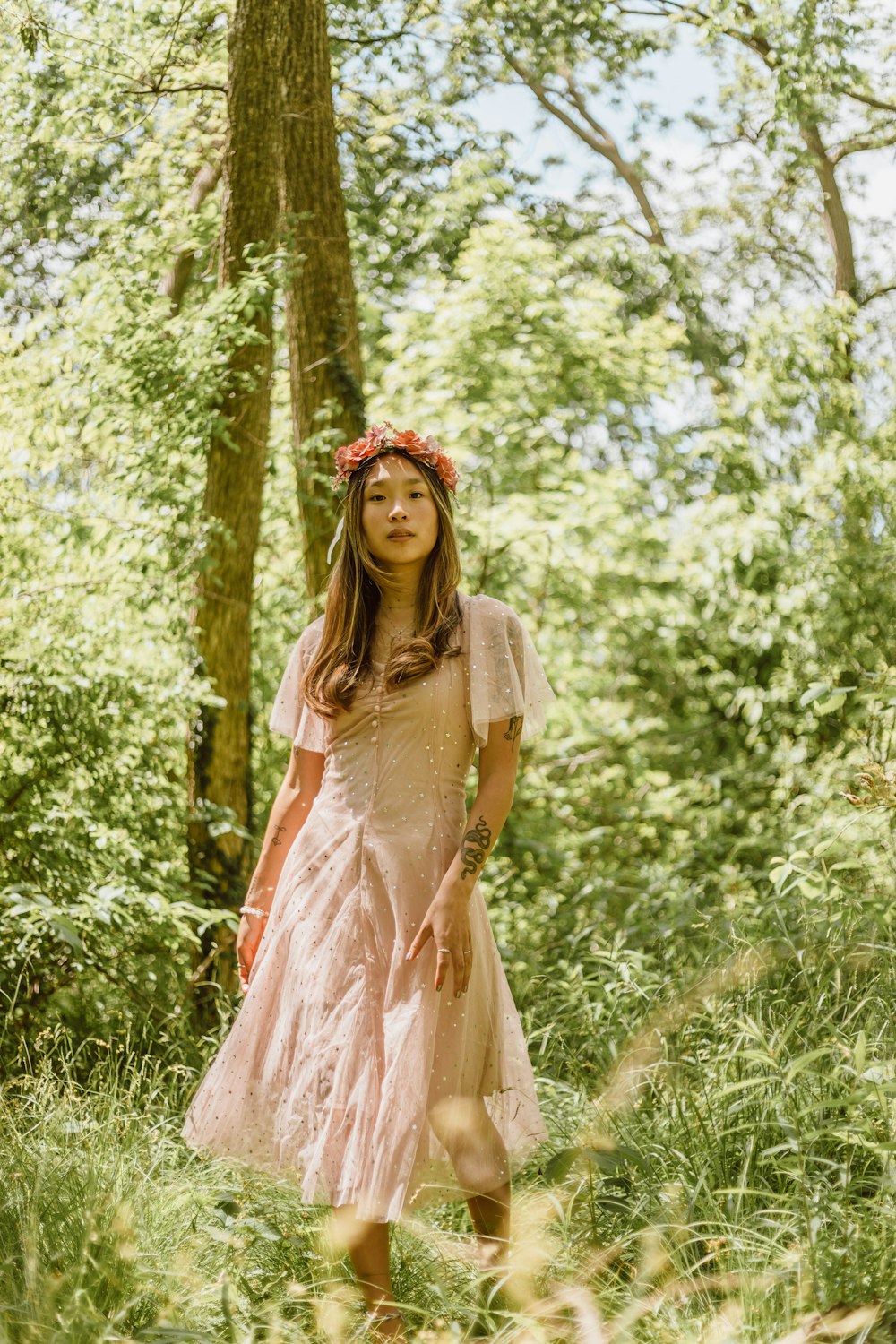 woman in beige dress standing near green trees during daytime