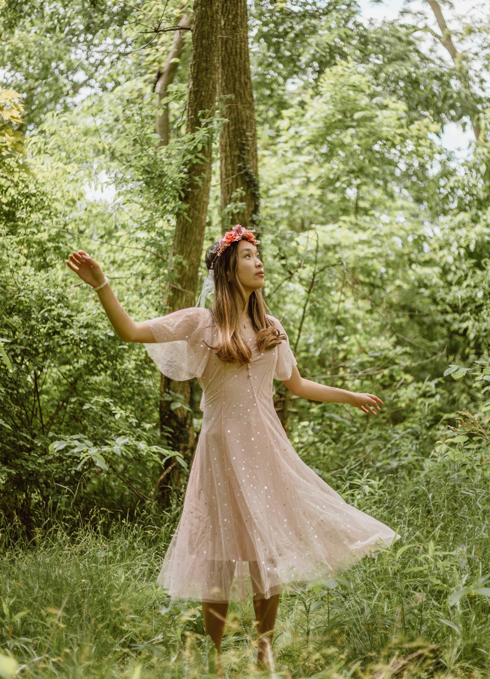 a girl in a pink dress standing in the woods