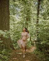 A woman in a flowing dress with subtle patterns, smiling while walking through a sunlit park.