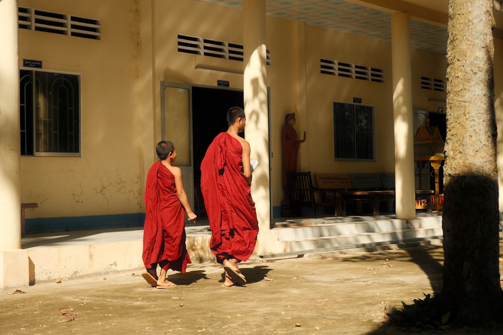 man in red thobe standing near yellow concrete building during daytime