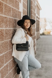A casually styled tote bag slung over a shoulder against an urban brick wall.