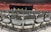 Rows of empty black chairs are neatly arranged in a large indoor arena with red stadium seating. A stage is set up at the front with a podium, potted plants, and flags. The words 'Class of' are partially visible on a sign, suggesting a graduation ceremony setting.