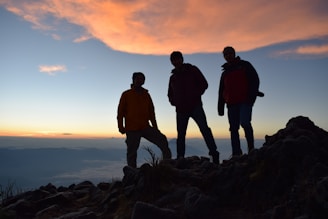 silhouette of 2 men standing on rocky shore during sunset