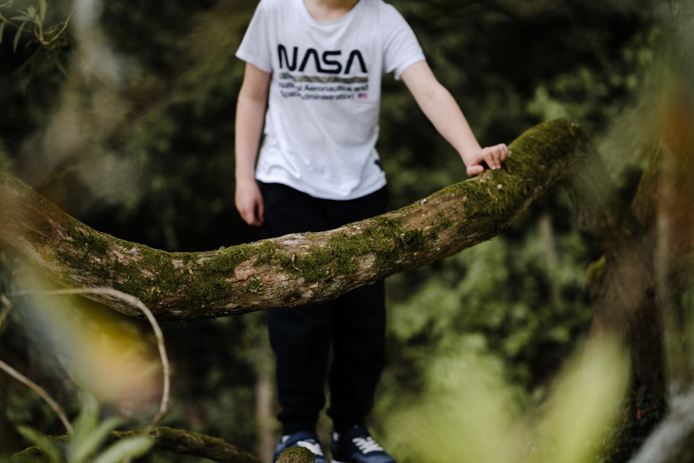 man in white crew neck t-shirt and black pants standing on brown tree branch during