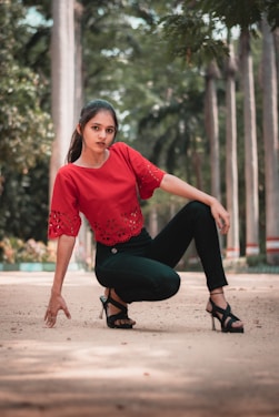 woman in red crew neck long sleeve shirt and black pants sitting on brown sand during