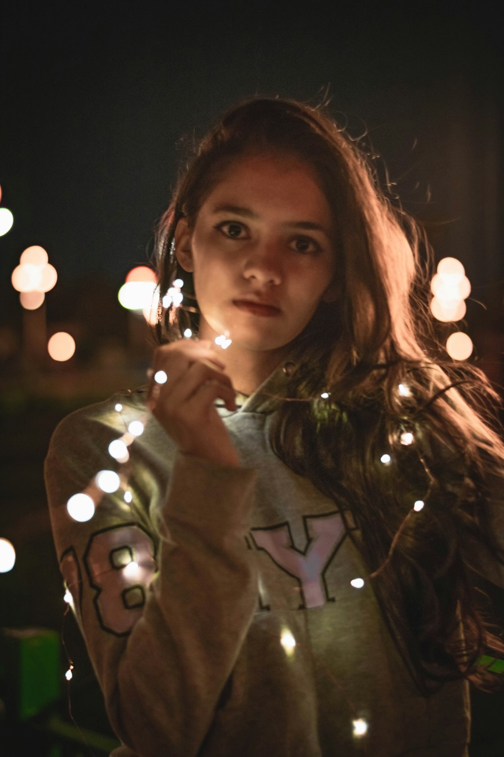 a girl is holding a lit up string of lights