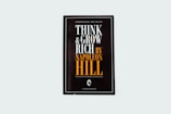 A black book cover titled 'Think and Grow Rich by Napoleon Hill' with the subtitle 'The secret to freedom and success.' The words are prominently displayed in white and orange fonts. The design is minimalistic with a modern aesthetic.