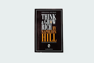 A black book cover titled 'Think and Grow Rich by Napoleon Hill' with the subtitle 'The secret to freedom and success.' The words are prominently displayed in white and orange fonts. The design is minimalistic with a modern aesthetic.