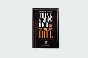 A black book cover titled 'Think and Grow Rich by Napoleon Hill' with the subtitle 'The secret to freedom and success.' The words are prominently displayed in white and orange fonts. The design is minimalistic with a modern aesthetic.