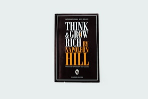 A black book cover titled 'Think and Grow Rich by Napoleon Hill' with the subtitle 'The secret to freedom and success.' The words are prominently displayed in white and orange fonts. The design is minimalistic with a modern aesthetic.
