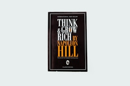 A black book cover titled 'Think and Grow Rich by Napoleon Hill' with the subtitle 'The secret to freedom and success.' The words are prominently displayed in white and orange fonts. The design is minimalistic with a modern aesthetic.
