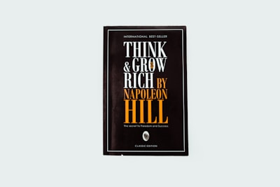A black book cover titled 'Think and Grow Rich by Napoleon Hill' with the subtitle 'The secret to freedom and success.' The words are prominently displayed in white and orange fonts. The design is minimalistic with a modern aesthetic.