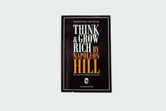 A black book cover titled 'Think and Grow Rich by Napoleon Hill' with the subtitle 'The secret to freedom and success.' The words are prominently displayed in white and orange fonts. The design is minimalistic with a modern aesthetic.
