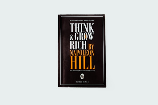 A black book cover titled 'Think and Grow Rich by Napoleon Hill' with the subtitle 'The secret to freedom and success.' The words are prominently displayed in white and orange fonts. The design is minimalistic with a modern aesthetic.