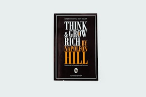 A black book cover titled 'Think and Grow Rich by Napoleon Hill' with the subtitle 'The secret to freedom and success.' The words are prominently displayed in white and orange fonts. The design is minimalistic with a modern aesthetic.