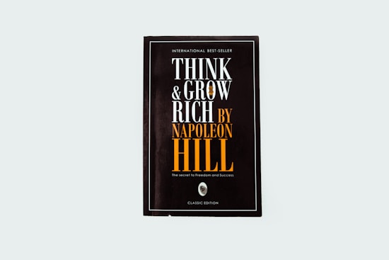A black book cover titled 'Think and Grow Rich by Napoleon Hill' with the subtitle 'The secret to freedom and success.' The words are prominently displayed in white and orange fonts. The design is minimalistic with a modern aesthetic.