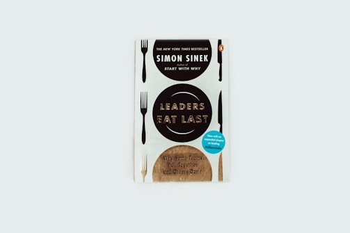 A book cover featuring the title 'Leaders Eat Last' by Simon Sinek. The design incorporates forks and knives along the edges, with informative text about the book's bestseller status and additional chapters included.