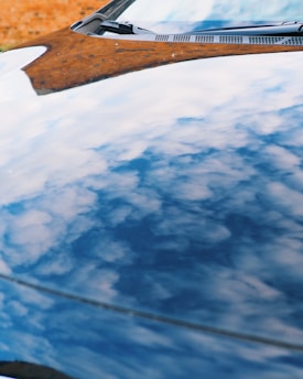 Reflection of a cloudy sky on the shiny surface of a car hood with a hint of a brick wall in the background.