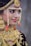 A person is adorned in elaborate traditional jewelry, featuring gold, red, and pearl elements. The jewelry includes a detailed headpiece, large earrings, a nose ring, and a heavily decorated necklace.