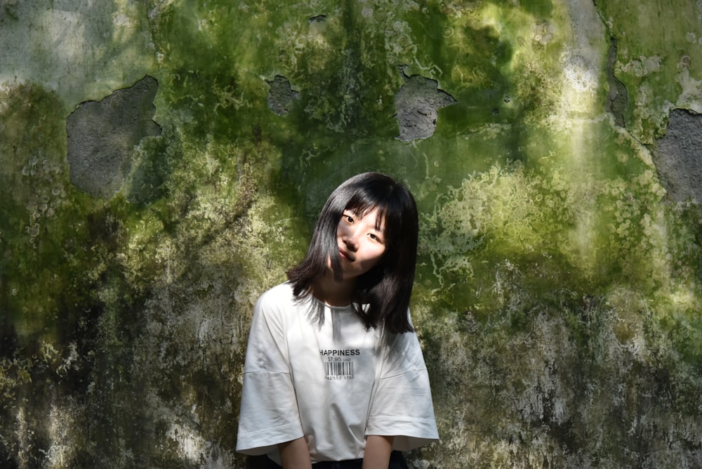 a woman standing in front of a moss covered wall