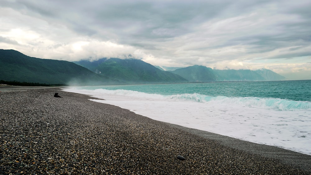 body of water near mountain under cloudy sky during daytime