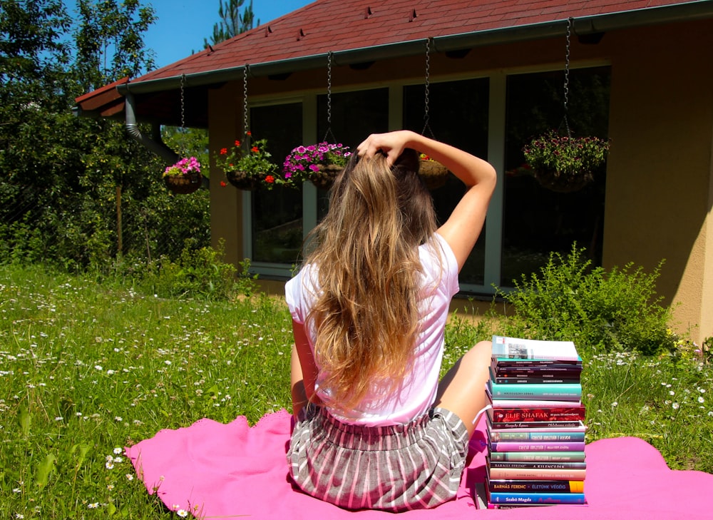 a woman sitting on a blanket with a stack of books