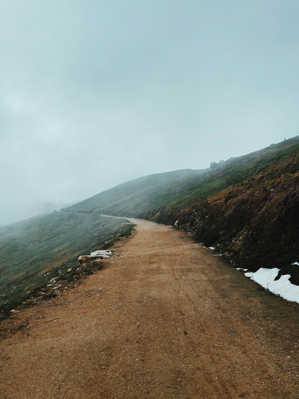 estrada de terra marrom perto da montanha verde sob nuvens brancas durante o dia