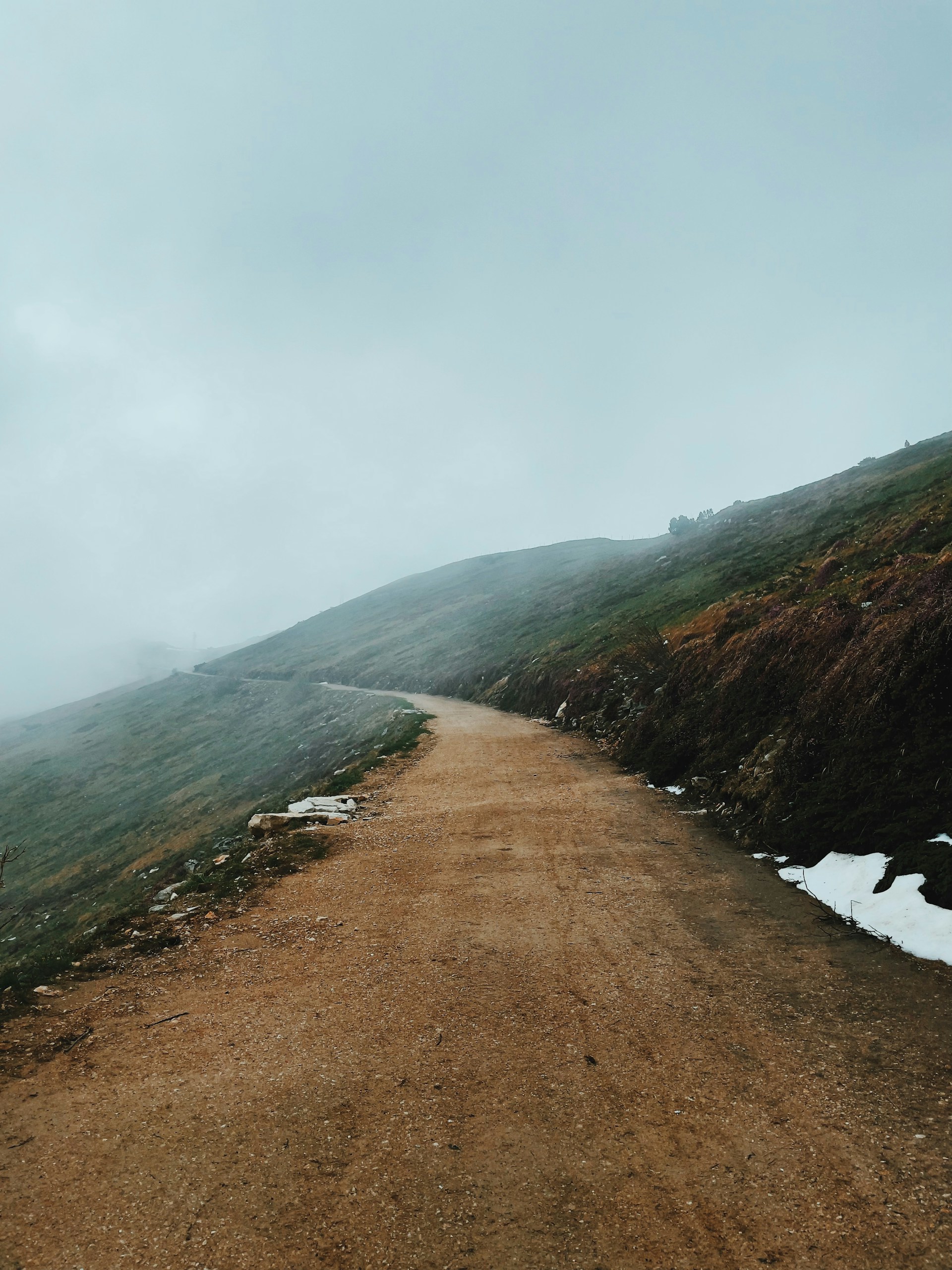 brown dirt road near green mountain under white clouds during daytime