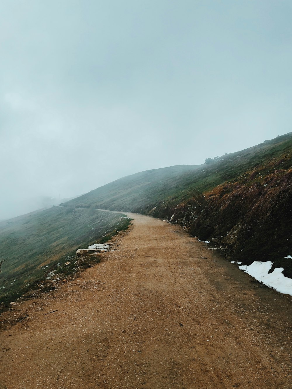 brown dirt road near green mountain under white clouds during daytime