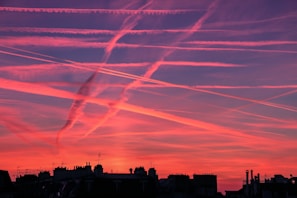 Time-lapse style photo showing chemtrails spreading and lingering above a city skyline during the day