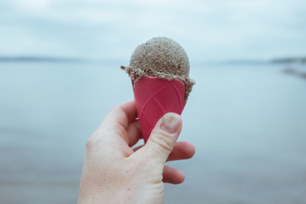 uma mão segurando um cone de sorvete na frente de um corpo de água