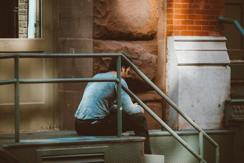 man in blue long sleeve shirt and gray pants sitting on gray concrete staircase