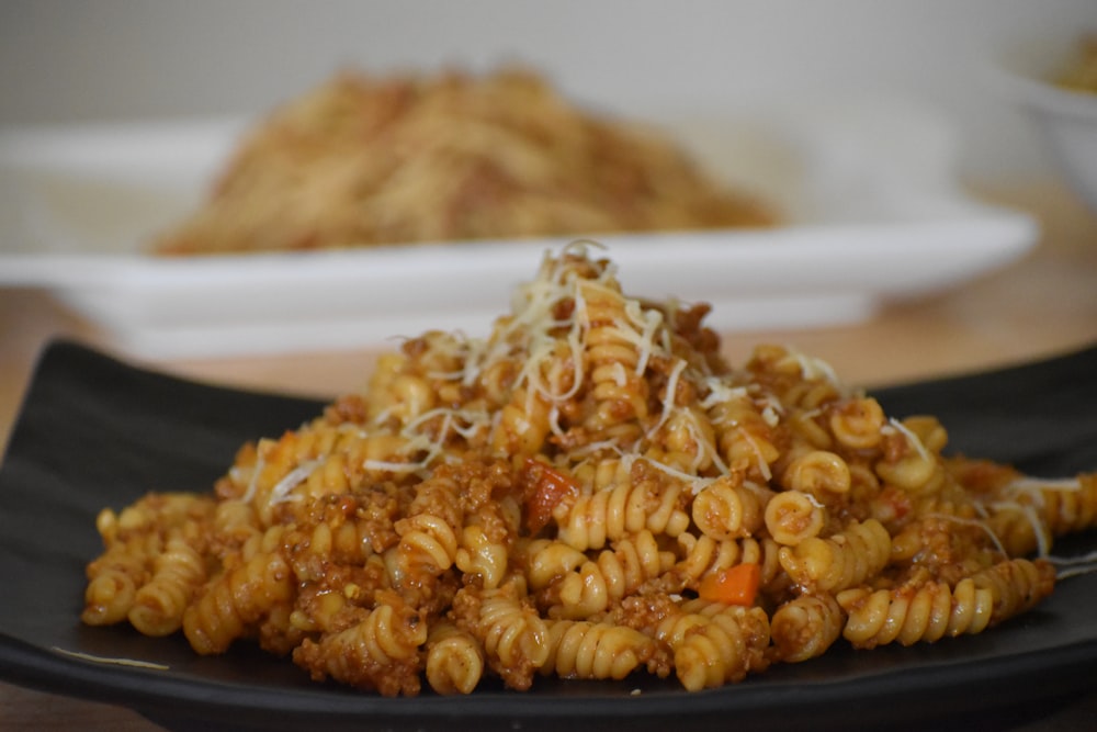 a black plate topped with pasta covered in sauce