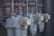 Several industrial gas meters and pipes are mounted on a metal structure. The meters are arranged in a row and connected to a network of thick pipes above. The overall industrial setting appears organized and functional.