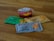 A selection of Nando's sauce packets and a small tub of Nando's Chilli Jam are placed on a wooden surface. The sauce packets include flavors such as Wild Herb, Medium, and Garlic in colorful packaging.