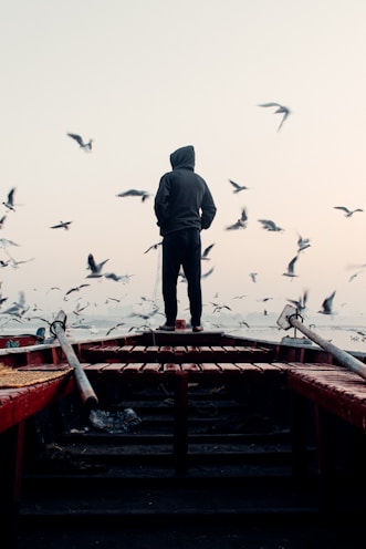 a man standing on top of a boat surrounded by seagulls