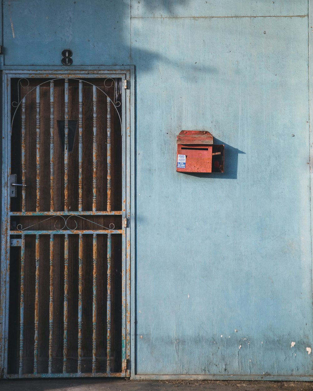 a blue wall with a rusted iron gate and a mailbox on it